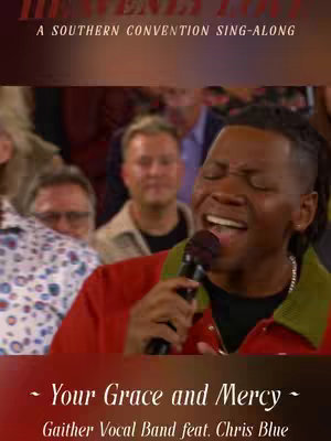 A man with dreadlocks, wearing a red shirt and a green jacket, is singing into a microphone. The background is blurred with other people, suggesting a live performance or recording.
