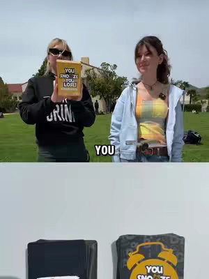 Two young women stand outdoors on a sunny day. One on the left holds a yellow box with text, while the other smiles and looks toward the camera. Lush green grass and trees form the background. The text "YOU" is placed in the lower part of the video.