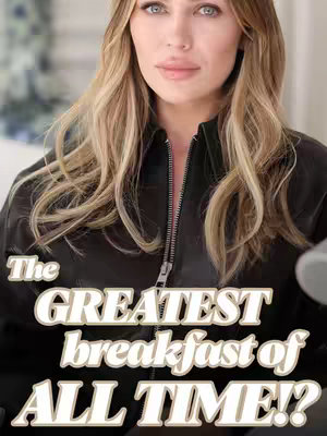 A medium shot featuring a woman centered in the frame. She has long, blonde hair and blue eyes, looking directly at the camera. She's wearing a black, zipped-up leather jacket. Bold text overlayed on the image reads "The GREATEST breakfast of ALL TIME!?"