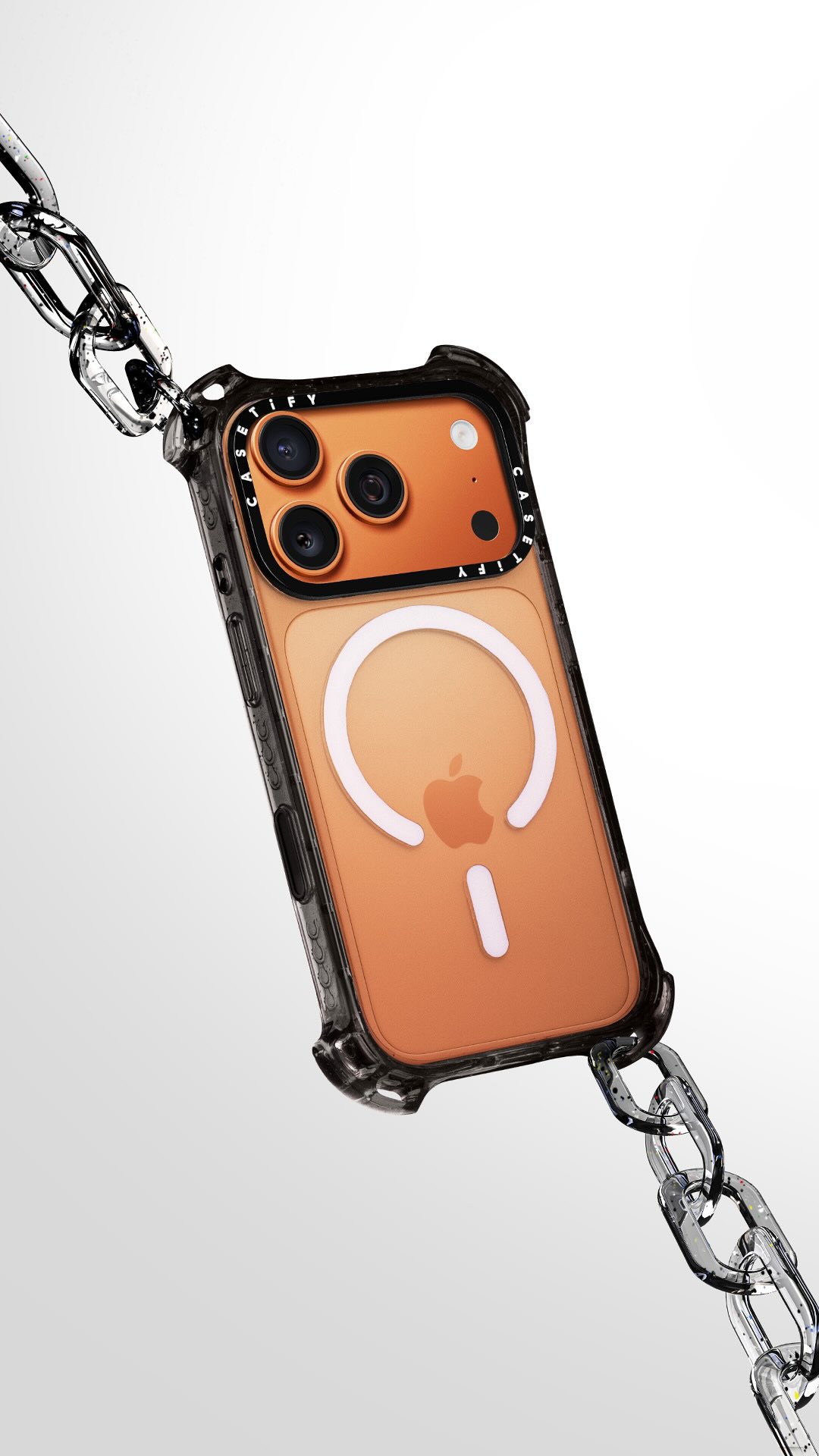 The image showcases an iPhone case suspended in mid-air, connected to a chain. The case is clear with black accents. The background is a gradient of gray to white, providing a clean and modern setting. The lighting is bright, highlighting the reflections on both the chain and phone case.