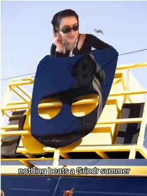 A woman is standing on top of a large, yellow structure with a stylized, blue shape resembling a mask in front of her. She is wearing sunglasses and a black top, with the sky as a backdrop and a hook at the bottom that states, 'nothing beats a Grindr summer'.