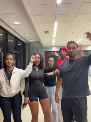The cover image features a group of five young adults, three women and two men, standing indoors in what appears to be a hallway or common area. They are all smiling and raising their hands in a celebratory or energetic gesture. The background is neutral, with light-colored walls and dark accents. The overall composition is casual and friendly, suggesting a fun or social gathering.