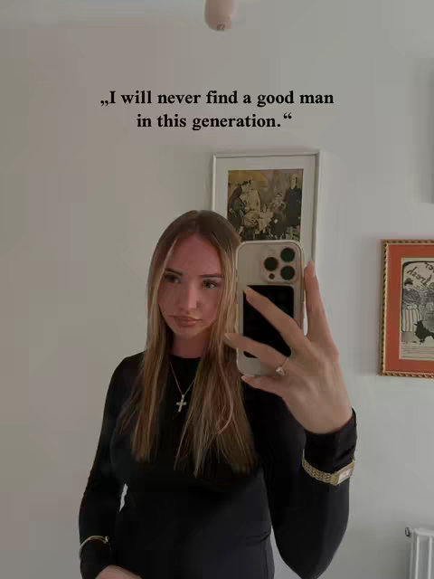 A young woman is taking a selfie in front of a white wall. She is wearing a black dress and a necklace with a cross pendant. The image has text overlayed that says, “I will never find a good man in this generation.” The selfie is mirrored.