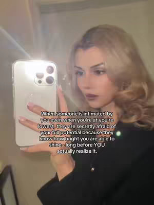 A woman with blonde hair is shown in a mirror selfie. She holds a smartphone, partially obscuring her face. Text overlayed on the image discusses a message about being intimitated by someone.