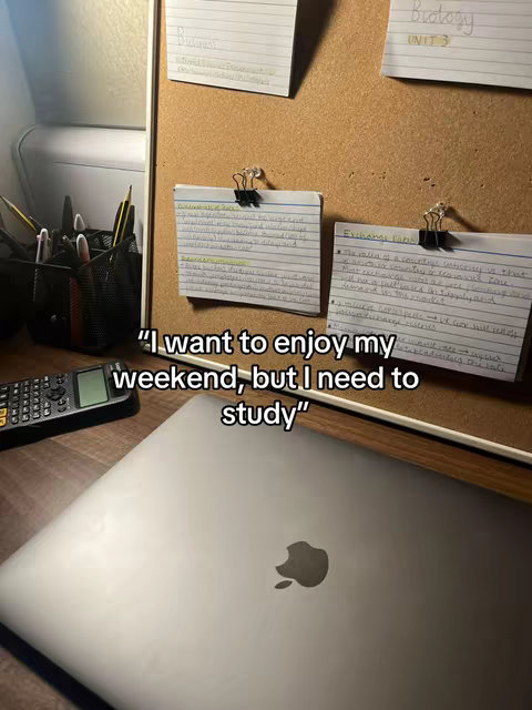 A desk setup with a laptop, calculator, and index cards pinned to a corkboard. Text overlay reads "I want to enjoy my weekend, but I need to study".
