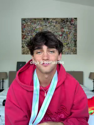 The cover image shows a young man in a red hoodie, posed in front of a wall with an abstract painting and a bedroom setting. He has a necklace, and a white sash is around his neck. Text overlay reads: "déjà 3 semaines".