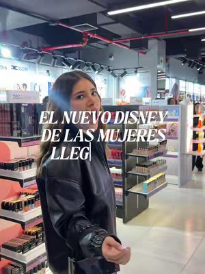A woman stands in a beauty store, looking towards the camera. The store is brightly lit with makeup and skincare products on display. Overlaid on the image is the text: "EL NUEVO DISNEY DE LAS MUJERES LLEG |."