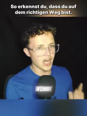 A young man with curly hair and glasses is shown against a dark background, speaking into a microphone. Text overlay is present at the top.