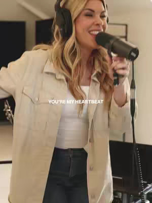 A woman with blonde hair is holding a microphone and singing into it. The background is a recording studio. The text overlay says, 'YOU'RE MY HEARTBEAT'.