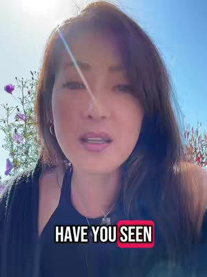 A woman with brown hair is centered in the frame, slightly angled to the viewer. The background is a soft blue sky with hints of sunlight. Partially visible behind her are green plants with a few purple flowers. A text overlay at the bottom reads 'HAVE YOU SEEN' in white with a red border.