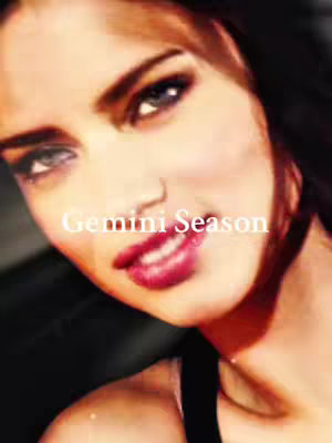 The image is a close-up of a woman's face, with a soft, blurred background. The woman has light skin, dark eyebrows, and dark eyes. The lighting highlights her facial features, with a focus on her lips, which are a vibrant shade of red. Text overlayed on the image reads "Gemini Season".