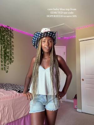 A woman with long braids is wearing a cowboy hat with a star pattern, a striped top, and denim shorts. She is standing in a bedroom with pink LED lights around the ceiling. Text overlays her head displaying a shopping promotion.