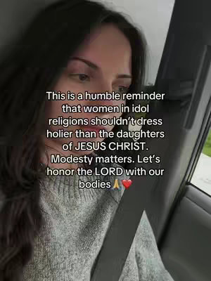 The image is a medium shot featuring a woman inside a car. She is positioned slightly off-center to the left, with her face and upper body visible. She has dark hair and is wearing a gray sweater. The background includes the car's interior, with a seat and a view of the outside visible through the window. Overlaid on the image is white text that emphasizes the importance of modesty within the context of religious beliefs.