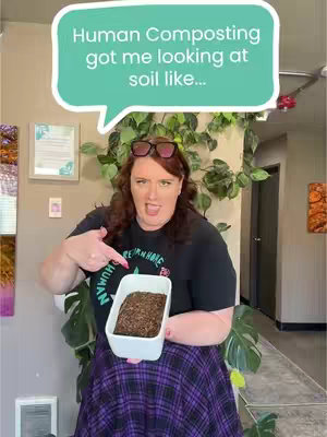 A woman with red hair and sunglasses perched on her head is holding a white rectangular container with soil. She is pointing to the soil with her left index finger, with an exaggerated expression. A text bubble above her says 'Human Composting got me looking at soil like...'. The background includes indoor plants and a wall.