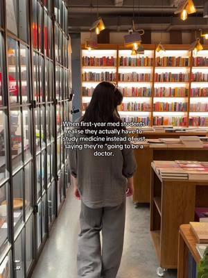 A person, likely a student, is walking away from the camera through a bookstore. The shelves are filled with books, indicating a scholarly environment. The lighting is warm.