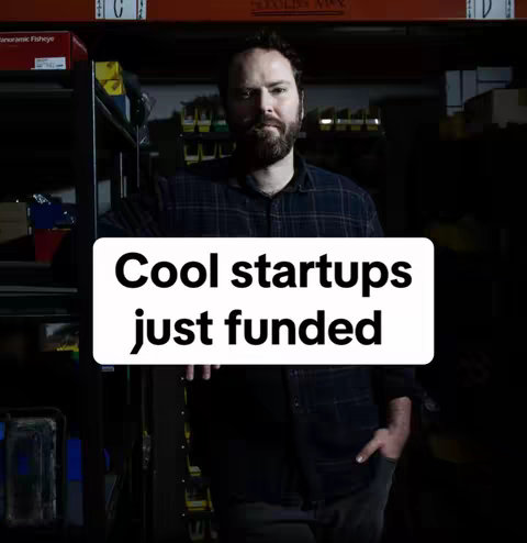 A man with a beard in a dark, cluttered storage room holds a white rectangle with bold black text. The background is a storage area with shelves filled with boxes and various items, creating a sense of an industrial or behind-the-scenes setting. The lighting is dim, with a bright spotlight illuminating the man and the text overlay, creating a contrast between the subject and the darkened background.