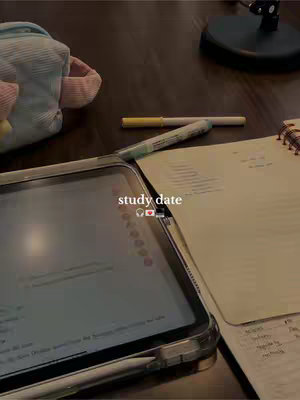 A photograph shows a desk with various items indicating a study session. An iPad is in the foreground, displaying a screen with text. A pencil and open notebook are next to it. Other desk items are in the background such as pens and bag.