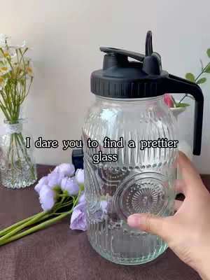 The cover image shows a clear glass jar with a black lid and handle, held by a person's hand. The jar is filled with an unknown substance. Decorative flowers are in the background. Text overlayed at the top states, 'I dare you to find a prettier glass'. The overall composition is clean and focuses on the product.