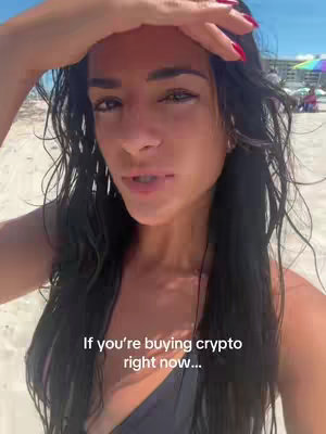 A young woman with long dark hair is on a beach under a bright sky. She's holding her hand up to shield her eyes from the sun, looking directly at the camera. Text overlayed on the image reads, "If you're buying crypto right now..."