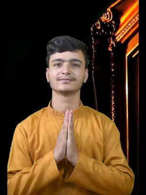 A young man wearing a golden-yellow outfit stands centered in the frame, offering a slight smile with his hands pressed together in a prayer or namaste position. The background is a dark black, with a blurred golden ornate structure to the right, like a decorative arch or a part of a temple, enhancing the spiritual theme.