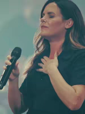 The cover image shows a woman with long, dark hair, a black long-sleeved top; a microphone in her left hand while her right hand is on her chest and her eyes closed; the background is a blurred light green.