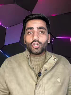 A mid-shot of a man speaking directly to the camera. He has short, dark hair, a neatly trimmed beard, and is wearing a neutral-toned jacket over a sweater. The background is a geometric design with shades of black, purple, and pink, lit to create a futuristic look.