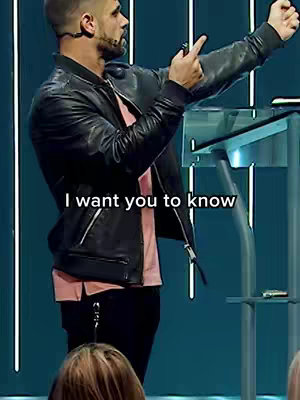 A man in a black leather jacket stands at a podium, gesturing with his hand as text overlays appear, all against a teal background.