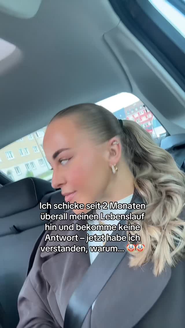 A selfie-style video taken from inside a car. A woman with blonde hair pulled back in a ponytail looks towards the camera. Text overlayed on the image in white
