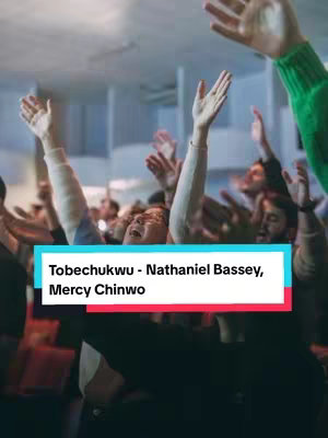 The image shows a group of people in a worship setting, with many arms raised in the air. The background suggests a church or auditorium environment. A text overlay in a rectangular box identifies the song and artists.