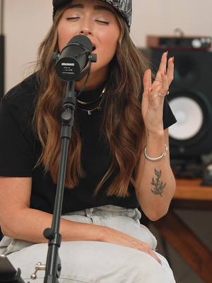 The cover image showcases a woman singing into a microphone, her eyes closed in concentration. She's wearing a black top and a patterned hat. A tattoo is visible on her arm, and jewelry adorns her neck and wrists.