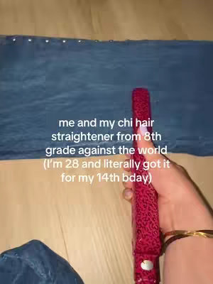 The image shows a person's hand holding a red and black patterned hair straightener against a background of a blue sheet folded over the floor. Text is overlaid on the image.