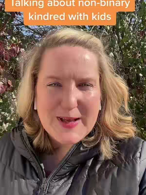 A selfie-style video featuring a woman with blonde hair and white earbuds, shot from the chest up. She's set against a blurry green and brown background of trees and foliage, with a text overlay at the top. The lighting suggests outdoor daylight.