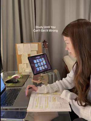 A person sits at a desk with a laptop, an iPad, and study materials. The person faces right, with text overlaid on the image.