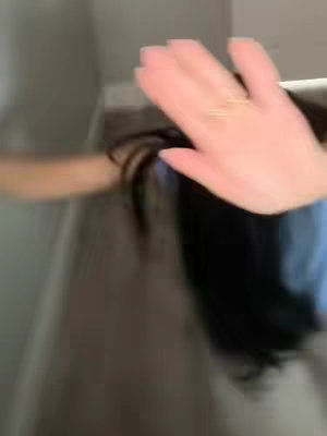 The image shows a hand in the forefront with a gold ring on a finger, slightly blurred. The hand is raised as if waving, and the arm and hair of a person are visible in the background, out of focus.