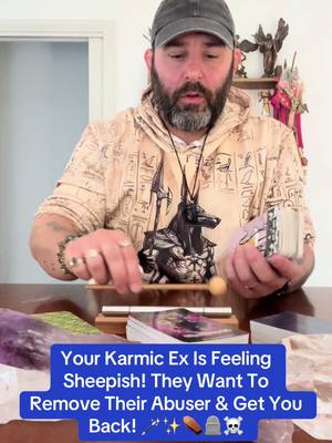 A man with a beard wearing a hoodie and a cap sits at a table with tarot cards, a mallet and other objects. Below is a blue rectangle with white text asking 'Your Karmic Ex Is Feeling Sheepish! They Want To Remove Their Abuser & Get You Back!' with some symbols.