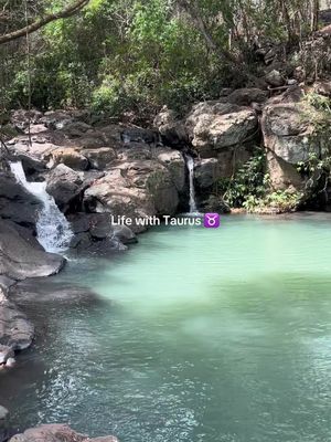 The image showcases a serene natural landscape featuring a waterfall cascading into a turquoise-colored pool, surrounded by rocky formations and lush greenery. The composition is centered on the water, suggesting a tranquil outdoor setting.