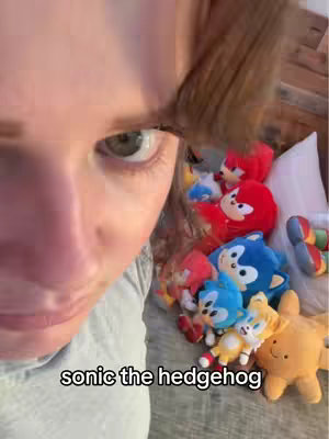 A person's face is prominently featured on the left side, with the upper portion mostly visible, and an eye is centrally focused. A collection of Sonic the Hedgehog plush toys is present in the background on the right, with the overlay text 'sonic the hedgehog'.