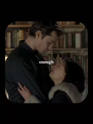 Two people, a man and a woman, are embracing in the foreground. The man is taller and mostly obscures the view of the woman. Behind them is a bookshelf.