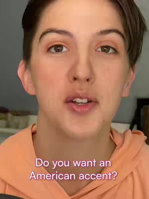 A close-up shot of a person with short hair, looking directly at the camera. The person has light skin, a neutral expression, and is wearing a light orange top. Text overlayed on the image reads, 'Do you want an American accent?'. The background is somewhat blurred, suggesting a home setting.
