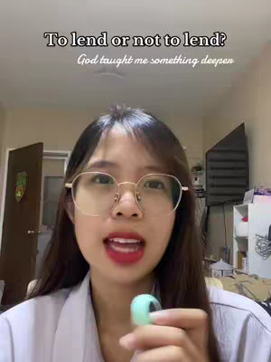 A woman with glasses and red lipstick is talking directly to the camera while holding a small object. Text overlays the image stating "To lend or not to lend? God taught me something deeper."