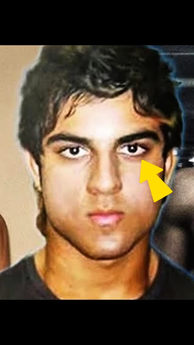 The image shows a close-up of a light-skinned man's face. He has dark hair, dark eyes, and a neutral expression. A yellow arrow points to his eye. The background is blurred and appears to be a mix of light and dark tones.