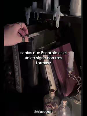 A dimly lit scene features a hand placing a book on a shelf filled with books, candles, and bottles. Text overlays in Spanish, with the account handle @hijasdegaia at the bottom.