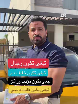 A man in a navy polo shirt stands in front of a house and a yellow car, with overlaid text in Arabic script.