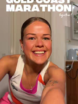 A selfie-style shot of a woman looking at the camera with a wide, happy smile. She has her hair pulled back and is wearing a pink and white athletic top. The image has text overlays: "Gold Coast Marathon" and "together!"