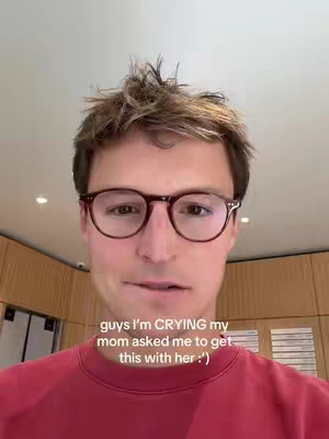 A close-up shot of a young man with brown hair and glasses, wearing a red shirt. He is indoors with a neutral background. The image includes overlay text at the bottom.