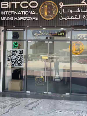 The cover image shows the storefront of a business called "BITCO INTERNATIONAL MINING HARDWARE" in Al Jaddaf, Dubai. The shop has large glass windows and doors, allowing a view of the interior; logos and contact information are posted on the glass. The image is taken in daylight, with sunlight reflecting off the glass.