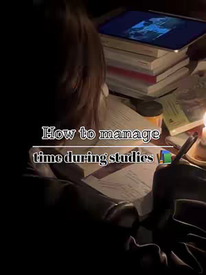 A dimly lit scene of a workspace. A person (likely female) is seated at a desk, seen from the back, with books, a tablet, and a lit candle. The lighting is warm, and the focus is on the study materials.