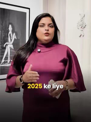 A woman with long dark hair and a maroon dress stands in an indoor setting. Behind her, there is a framed black and white drawing of a woman, and white decorated panel. The overlay text, "2025 ke liye", is placed at the bottom of the image.
