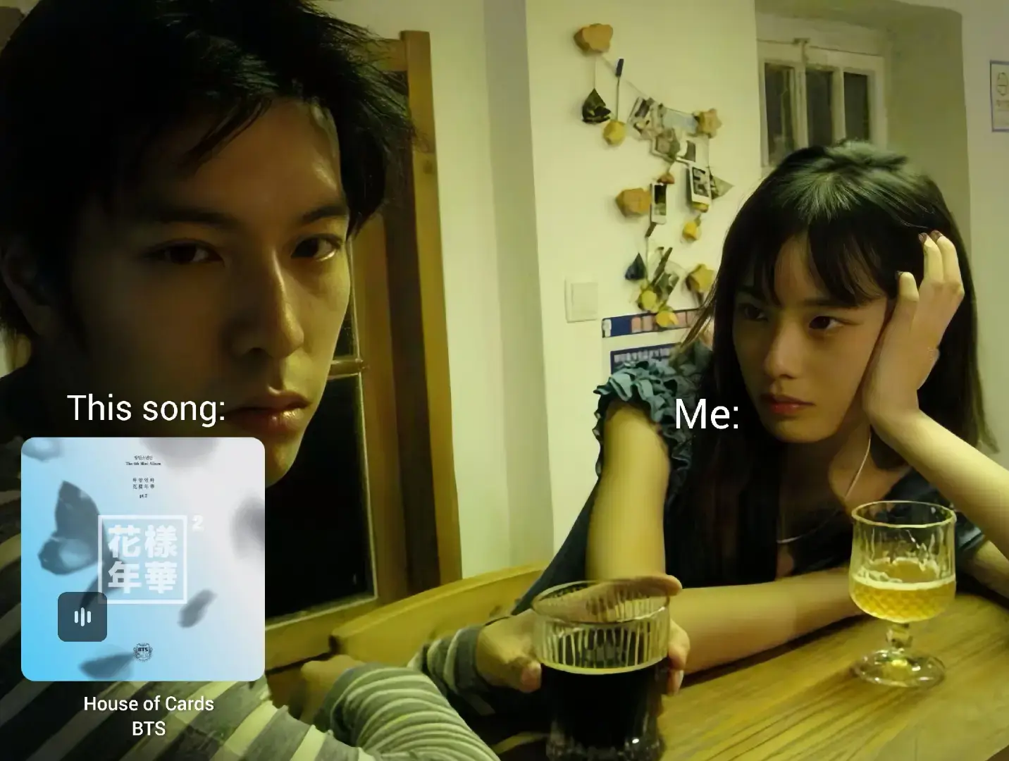 A split-screen meme-style image. On the left, a young man looks directly at the viewer with a serious expression. In front of him is a phone screen with a blue gradient interface displaying the album art for BTS' "House of Cards." The right side shows a young woman looking off to the side, with a thoughtful expression, holding a glass of beer. The background features a cozy, dimly lit interior with a wooden table.