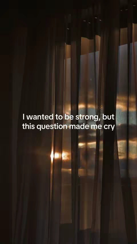 The image presents a vertically oriented composition with a muted color palette. The background features a series of dark brown vertical lines, resembling curtains or a textured wall. Light filters through from the right side, creating a warm glow and highlighting the textures. A text overlay appears in the center, written in a clean font, with the words 'I wanted to be strong, but this question made me cry'.